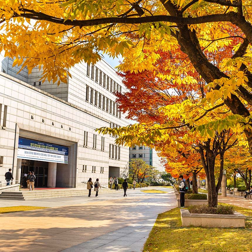 A wide campus plaza at Hanyang University with students walking past a modern building under trees with vibrant yellow and orange fall foliage.