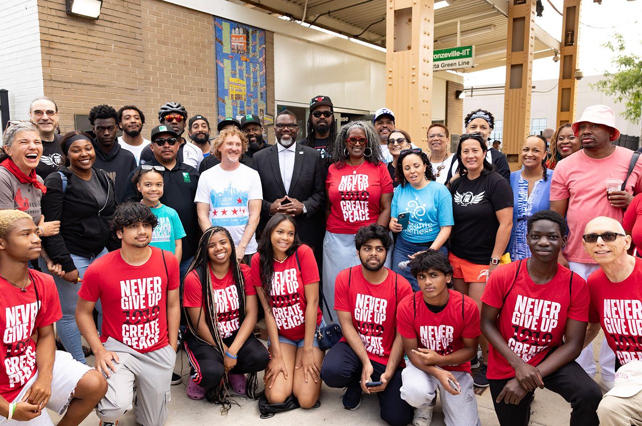 The justice ambassadors (kneeling, in red T-shirts) pose for a photo with Chicago Mayor Brandon Johnson outside the Green Line “L” elevated train stop where artwork was installed as a commemoration to the of Eugene Williams, whose death sparked the violence in summer 1919 in Chicago