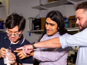 3 men in a lab pointing and looking at scientific instrument