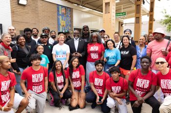 The justice ambassadors (kneeling, in red T-shirts) pose for a photo with Chicago Mayor Brandon Johnson outside the Green Line “L” elevated train stop where artwork was installed as a commemoration to the of Eugene Williams, whose death sparked the violence in summer 1919 in Chicago