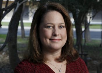 Nicole Beebe, a woman with brown hair wearing a patterned red shirt, smiles in a portrait with trees in the background