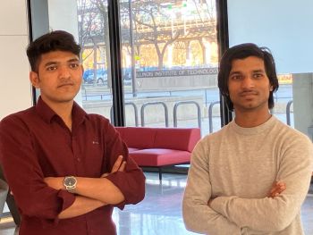 Two young men, one in a dark red button-down and the other in a gray crew-neck shirt, pose for a photo with their arms crossed.